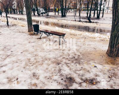 Primo piano di panca bagnata sulla strada all'inizio della primavera. Pew di legno in tempo snello con neve fusa Foto Stock