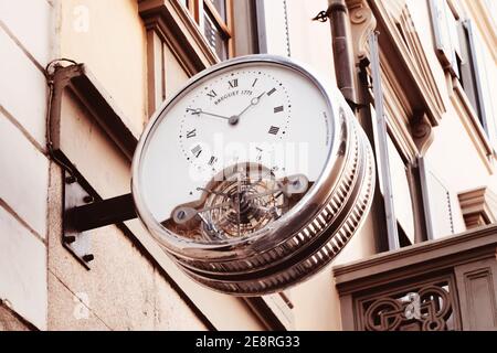 Orologio vintage con numeri romani appesi alle pareti dell'edificio nel centro della città europea. Orologi analogici per marciapiedi per esterni Foto Stock
