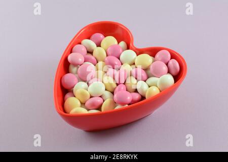 Spuntino al cioccolato rivestito di caramelle di San Valentino rosa, bianco  e giallo in ciotola a forma di cuore rosso su sfondo lavanda Foto stock -  Alamy