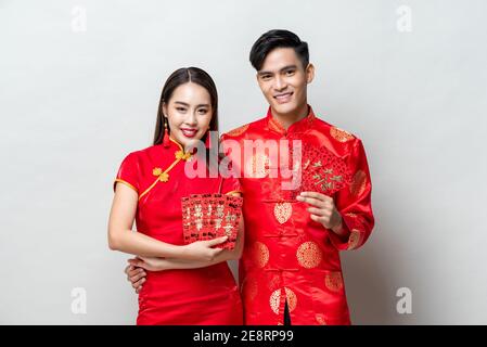 Felice coppia asiatica in costumi orientali tradizionali che tengono buste rosse o Ang Pao in grigio chiaro sfondo per i concetti cinesi nuovo anno, testi me Foto Stock