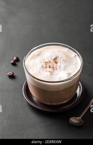 Primo piano sul caffè del cappuccino. Caffè fresco con deliziosa schiuma di latte e cannella su tavolo scuro. Foto Stock