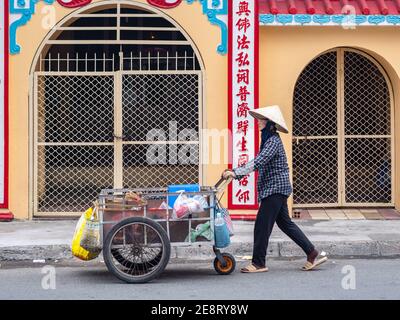 Donna vietnamita che spinge un carro di fronte ad un santuario buddista nella città di ho Chi Minh, Vietnam. Foto Stock