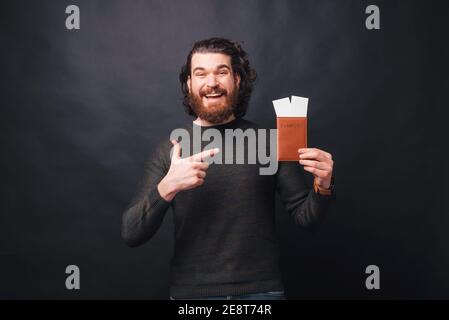 Un giovane allegro sta tenendo un passaporto con due biglietti in esso e indicando che sta sorridendo alla macchina fotografica. Foto Stock