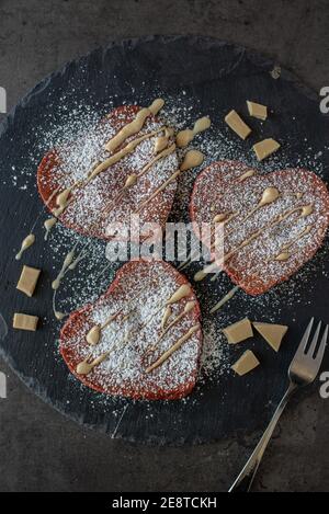 frittelle di velluto rosso a forma di cuore su un tavolo Foto Stock