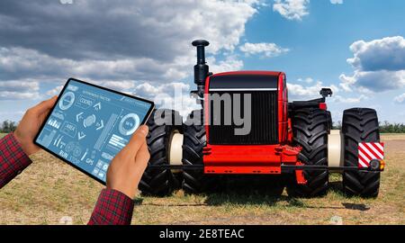 Un agricoltore con tavoletta digitale controlla un autonomo del trattore su una smart farm Foto Stock