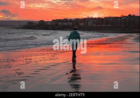 Portobello, Edimburgo, Scozia, Regno Unito. 1 febbraio 2021. Breve e sorprendente alba da accogliere a febbraio. Nella foto: Donna che cammina lungo la riva del Firth of Forth. Foto Stock