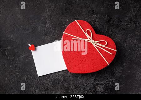 Scatola regalo a forma di cuore rosso, rose, carta messaggio vuota su un tavolo nero grunge. San Valentino sfondo. Foto Stock