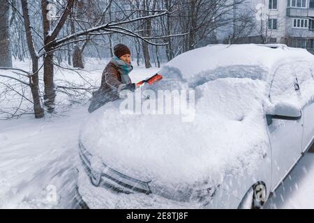 Donna conducente pulisce il parabrezza della sua auto dalla neve. Guida di un'auto in inverno Foto Stock