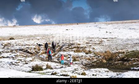 Una vista panoramica di una famiglia godendo di una passeggiata nella neve sul selvaggio e aspro Rough Tor su Bodmin Moor in Cornovaglia. Foto Stock