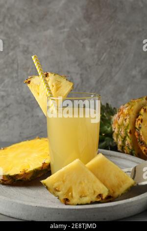 Vassoio con fette di ananas e bicchiere di succo di frutta grigio sfondo Foto Stock