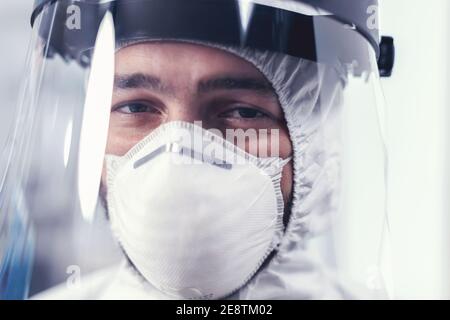 Primo piano di indossare la maschera facciale e il tuta ppe. Ricercatore overlavored vestito in tuta protettiva contro l'invasione con coronavirus durante l'epidemia globale. Foto Stock