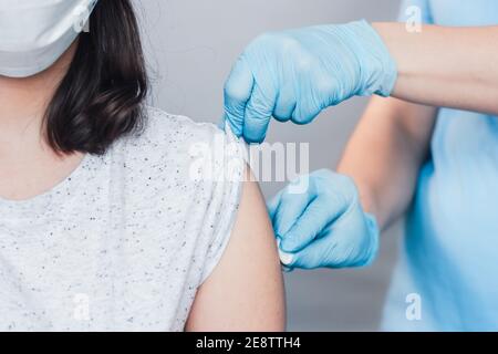prima di effettuare l'iniezione al paziente in una maschera medica, incura le mani in guanti medici utilizzando il cotone. Concetto di vaccinazione con coronavirus Foto Stock