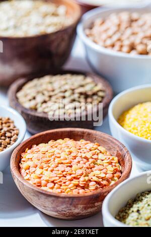 Cereali secchi assortiti e legumi in ciotole bianche e in legno, fondo bianco. Concetto di proteina vegana. Foto Stock