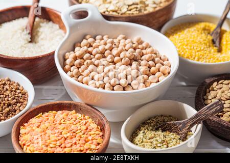 Cereali secchi assortiti e legumi in ciotole bianche e in legno, fondo bianco. Concetto di proteina vegana. Foto Stock