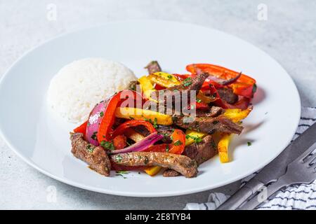 Concetto di cucina peruviana. Lomo saltado - pezzi di manzo fritti con peperoni, cipolle e patate su un piatto bianco. Foto Stock