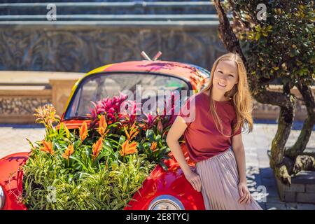 Elegante ritratto di bella moda donna ondulato luccicante zenzero capelli lunghi accanto rosso retro auto. Viaggiare in Europa dopo COVID-19 coronavirus Foto Stock