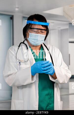 Donna asiatica medico con schermo facciale e guanti che tengono una siringa con entrambe le mani. Messa a fuoco selettiva. Concetto di vaccinazione e assistenza sanitaria.