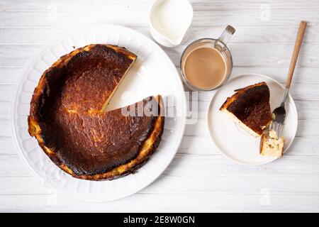 Cheesecake tradizionale basco bruciato con una tazza di caffè su un tavolo di legno bianco. Vista dall'alto Foto Stock