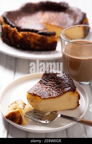 Cheesecake tradizionale basco bruciato con una tazza di caffè su un tavolo di legno bianco. Foto Stock