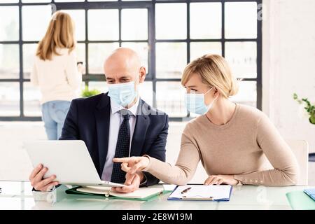 Gruppo di uomini d'affari che indossano maschere per il viso mentre lavorano insieme in ufficio. Riunione di affari. Foto Stock