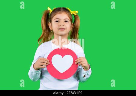 Ritratto di carino allegro affascinante attraente magnifica ragazza bello con pony-coda che tiene in mani grande carta cuore isolato su verde Foto Stock