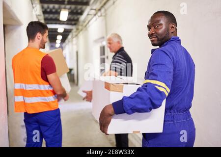 Il gruppo di lavoratori trasporta i pacchi attraverso la corsia nel magazzino di una fabbrica o di una società di spedizione Foto Stock