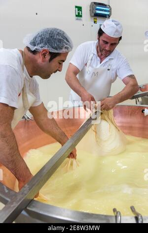 Un uomo mescolando il latte in un'iva rivestita di rame fare parmigiano reggiano di Parmigiano in uno stabilimento di Bologna Italia Foto Stock