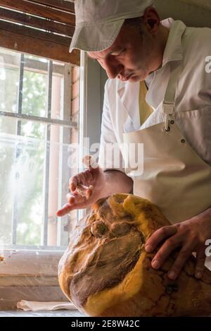 Un operaio in una fabbrica di prosciutto di parma aggiungendo grasso a mano per sigillare la carne prima di essere maturato Foto Stock