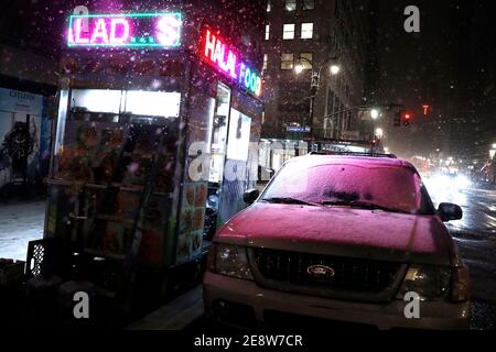 La luce viola riflette una neve coperta auto in Midtown.The neve inizia ad accumularsi come la prima Nor'pasqua del 2021 è proiettato a scaricare oltre due piedi di neve sulla città a metà giornata di domani e rastremarsi entro martedì. Foto Stock