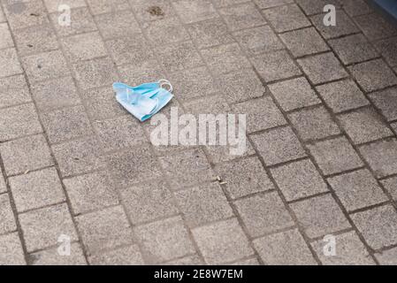 Una maschera medica usa e getta si trova nella polvere sul marciapiede. Foto Stock