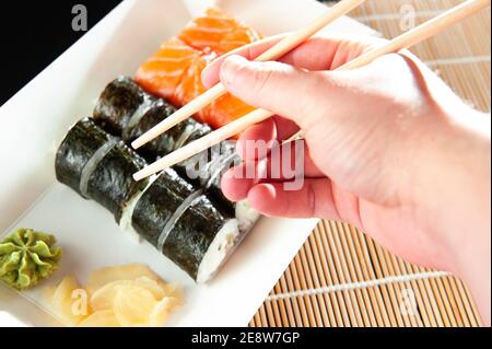 primo piano di bastoncini che prendono parte al sushi roll al ristorante che mangia il sushi roll utilizzando le bastoncini. Foto Stock