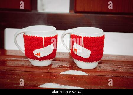 Tazze in coperte rosse a maglia con cuori con tè caldo e vapore. Il concetto di San Valentino Foto Stock