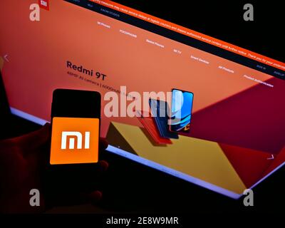 Vista ad alto angolo della persona che tiene il cellulare con il logo della società cinese di elettronica Xiaomi Corporation in esposizione. Mettere a fuoco lo schermo del telefono cellulare. Foto Stock