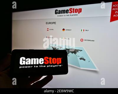 Persona che detiene il telefono cellulare con il logo della società al dettaglio GameStop Corp. (Videogiochi, elettronica di consumo) di fronte al sito web. Mettere a fuoco lo schermo del telefono. Foto Stock