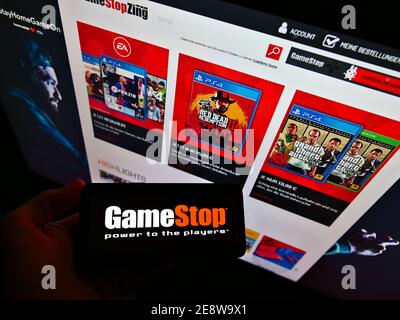 Persona che tiene lo smartphone con il logo della società di vendita al dettaglio GameStop Corp. Di fronte al sito web con negozio online. Mettere a fuoco lo schermo del telefono. Foto non modificata. Foto Stock