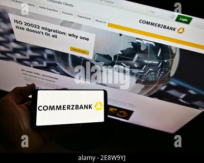 Persona che detiene smartphone con logo aziendale della banca universale tedesca Commerzbank AG in esposizione davanti al sito web della società. Mettere a fuoco lo schermo del telefono. Foto Stock