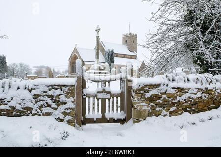 Chiesa di San Marys e porta nella neve. Swinbrook, Cotswolds, Oxfordshire, Inghilterra Foto Stock