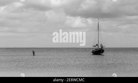 Barca a Vlieland. Queste navi a vela possono posare sulla sabbia a bassa acqua. Donna sta camminando dalla barca all'isola Foto Stock