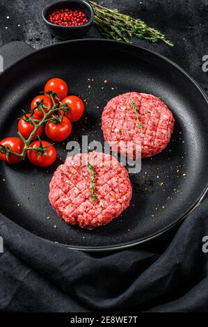 Cotolette grezze di carne di manzo tritata, patatine in una padella. Sfondo nero. Vista dall'alto Foto Stock