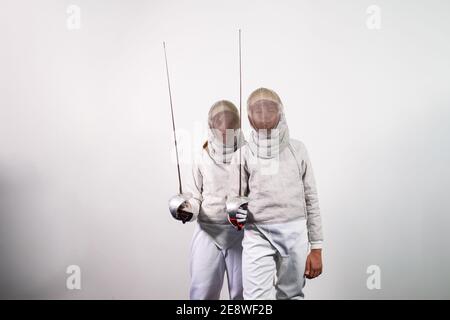 Ragazze adolescenti in costumi scherma con spade nelle loro mani isolate su sfondo bianco studio. I giovani praticano e praticano la recinzione. Sport, Foto Stock