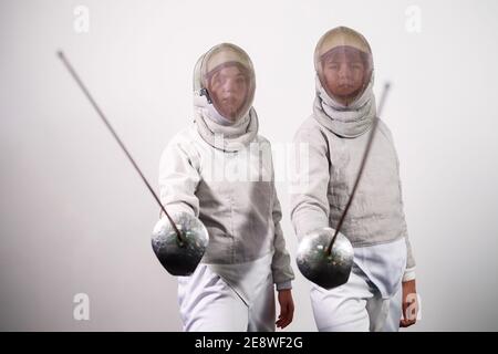 Ragazze adolescenti in costumi scherma con spade nelle loro mani isolate su sfondo bianco studio. I giovani praticano e praticano la recinzione. Sport, Foto Stock