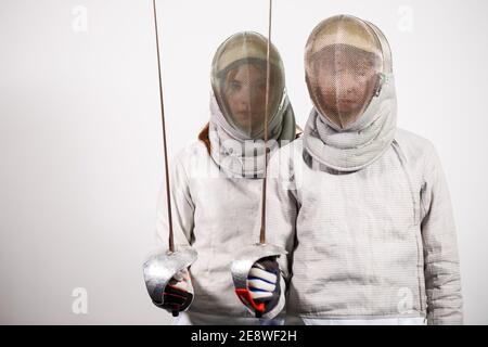 Ragazze adolescenti in costumi scherma con spade nelle loro mani isolate su sfondo bianco studio. I giovani praticano e praticano la recinzione. Sport, Foto Stock