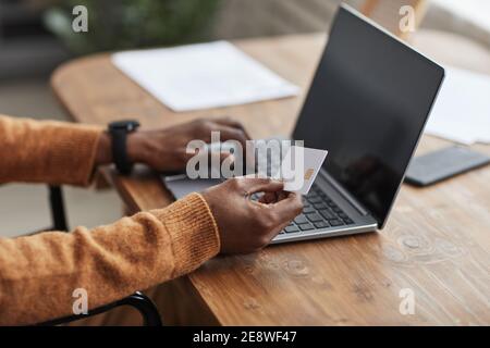 Primo piano di un uomo afroamericano irriconoscibile in possesso di carta di credito mockup, mentre lo shopping online via computer portatile, spazio di copia Foto Stock