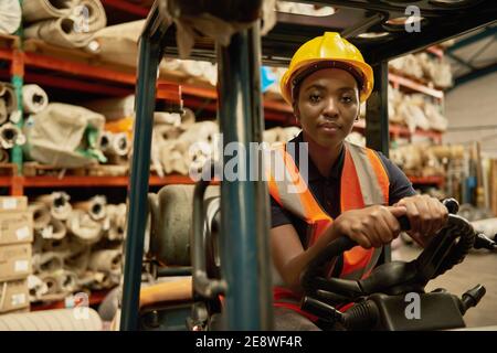 Fiducioso operatore africano di carrelli elevatori a forche che lavora in un magazzino Foto Stock