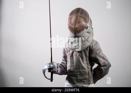 Una ragazza in un vestito da scherma con una spada in mano. Modello femminile giovane che pratica ed esercitandosi. Sport, stile di vita sano. Foto Stock