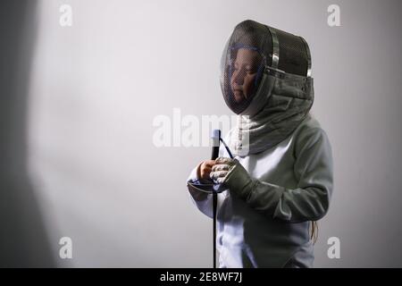 Una ragazza in un vestito da scherma con una spada in mano. Modello femminile giovane che pratica ed esercitandosi. Sport, stile di vita sano. Foto Stock