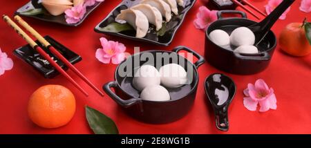 Zuppa cinese dolce con palle di riso e gnocchi per il quartiere a luci rosse. Dessert e spuntini tradizionali Cinesi di Capodanno. Cena di festa su sfondo rosso. Banner, formato lungo. Foto Stock