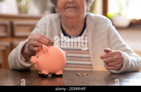 Donna anziana che mette una moneta in una banca piggy Foto Stock