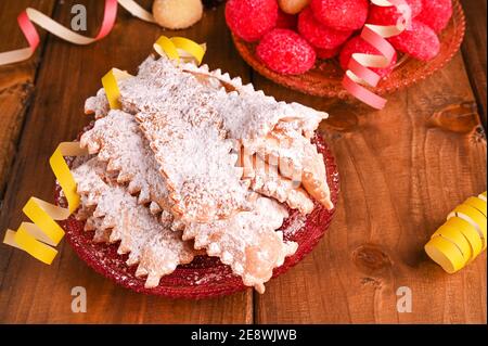 Carnevale cibo TIPICO e confetti. Frappole o chiachiere o ali d'angelo e caffè aromatico su uno sfondo legnoso. Pasta dolce tradizionale fritta e cosparsa di zucchero in polvere. Foto Stock