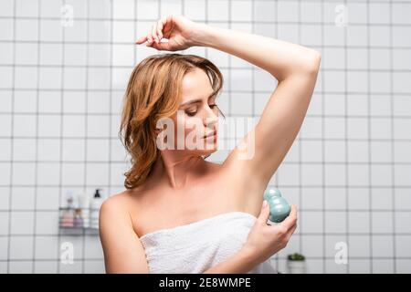 donna in asciugamano bianco che applica un rotolo deodorante in bagno moderno Foto Stock